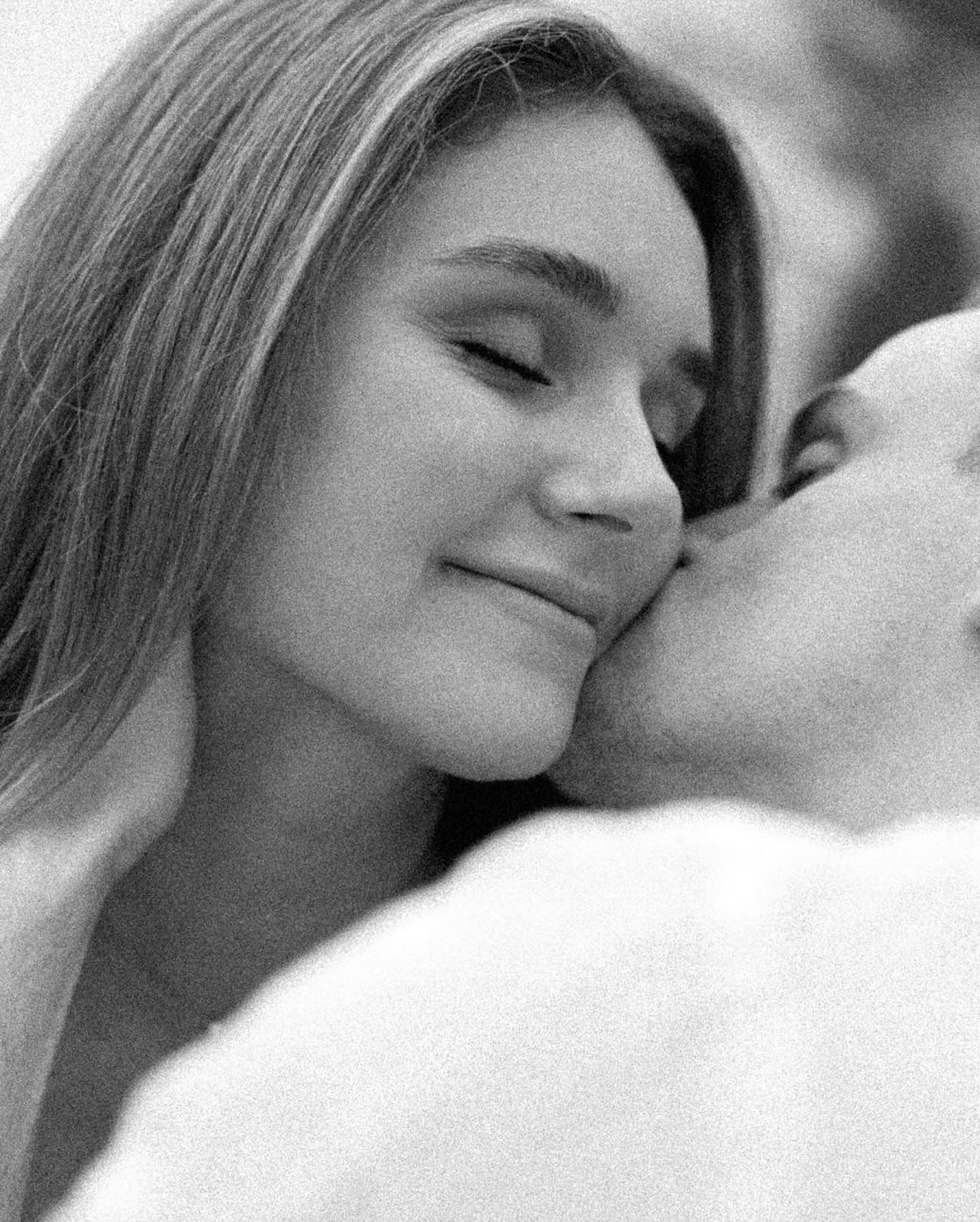 Black and white photo of a tender kiss on the cheek, Caitlin smiling with eyes closed.